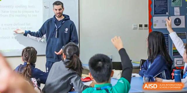 A teacher at Harrow International School Beijing (AISL Beijing) is leading a classroom discussion with a student raising their hand.