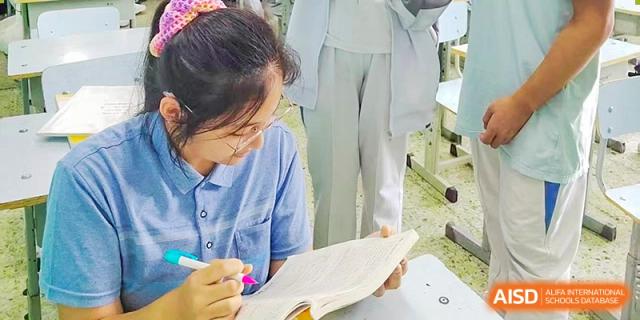 A student from Harrow International School Beijing (AISL Beijing) is intently writing notes in a book during a class.