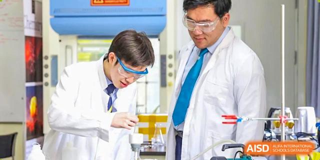 Two male students from Harrow International School Beijing (AISL Beijing), wearing lab coats and goggles, are working together on a science experiment.