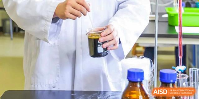 A student from Harrow International School Beijing (AISL Beijing) is carefully pouring a dark liquid during a chemistry experiment.