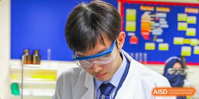 A close-up shot of a male student from Harrow International School Beijing (AISL Beijing) wearing safety goggles while concentrating in a science lab.