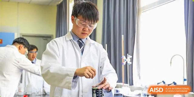 A student from Harrow International School Beijing (AISL Beijing) in a lab coat and goggles is mixing a substance in a beaker.