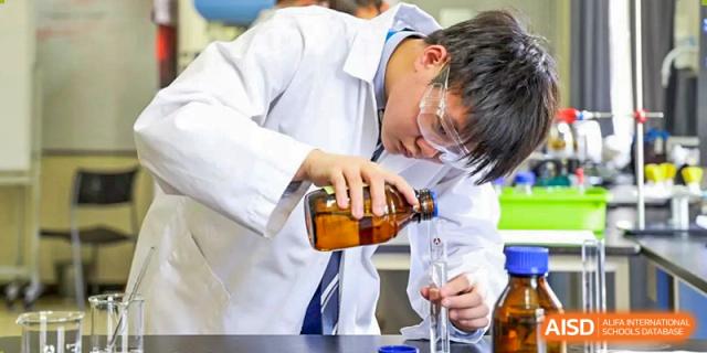 A male student from Harrow International School Beijing (AISL Beijing) is pouring a substance from a large bottle into a beaker in the school lab.
