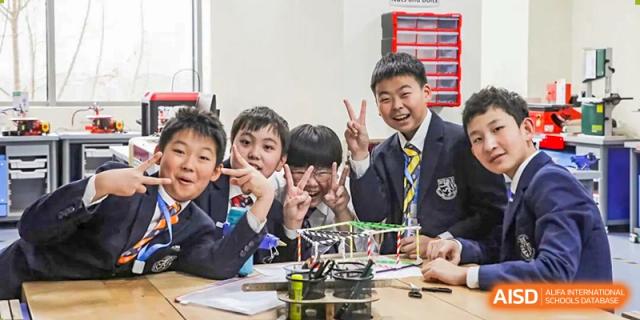 A group of students from Harrow International School Beijing (AISL Beijing) are smiling and posing with their robotics or engineering project at a table.