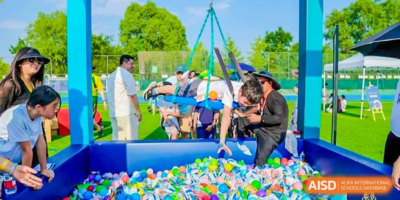 A group of students and teachers from Harrow International School Beijing (AISL Beijing) are gathered around a ball pit and swing at an event.