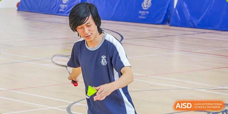 A student from Harrow International School Beijing (AISL Beijing) is actively participating in a sports activity, holding a shuttlecock and racket on a court.