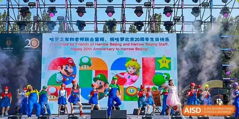 Students from Harrow International School Beijing (AISL Beijing) are performing on a brightly lit stage with colorful backdrops featuring Mario characters, likely for an anniversary celebration or school show.