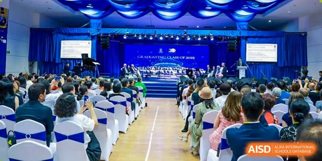 A large audience is seated in an auditorium, attending an event at Harrow International School Beijing (AISL Beijing) with a stage illuminated in blue.