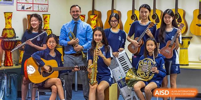 The music ensemble of Harrow International School Beijing (AISL Beijing), including students with guitars and wind instruments, poses with their teacher.