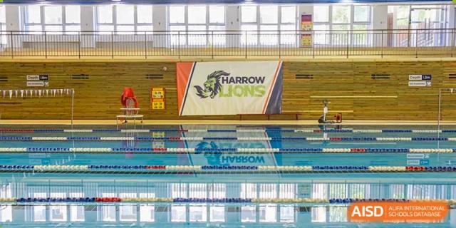The indoor swimming pool at Harrow International School Beijing (AISL Beijing) is shown with the school's 'Harrow Lions' logo displayed on the wall.