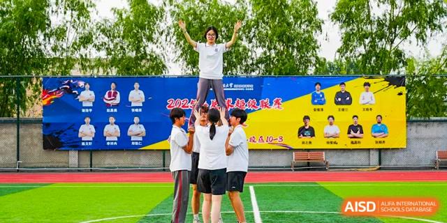 A male student celebrating with arms raised while being held up by a group of students during a sports day event at BEIJING CHAOYANG TONGWEN FOREIGN LANGUAGE SCHOOL.