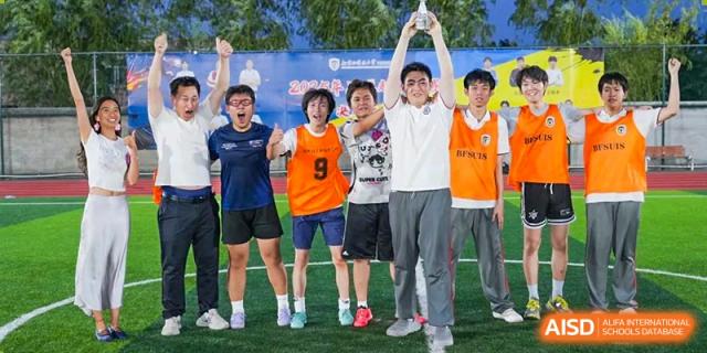 A group of male students in sports jerseys cheering together and holding up a trophy on a sports field at BEIJING CHAOYANG TONGWEN FOREIGN LANGUAGE SCHOOL.