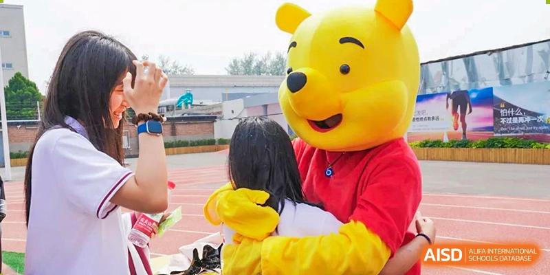 A student hugging a large, friendly yellow bear mascot during an outdoor event at BEIJING CHAOYANG TONGWEN FOREIGN LANGUAGE SCHOOL.