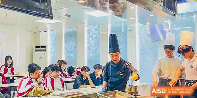 A close-up shot of students observing a chef in a black uniform demonstrating cooking or culinary skills at BEIJING CHAOYANG TONGWEN FOREIGN LANGUAGE SCHOOL.