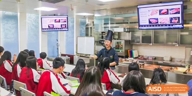 Students sitting around a table in a modern kitchen or nutrition classroom watching a chef give a lesson at BEIJING CHAOYANG TONGWEN FOREIGN LANGUAGE SCHOOL.