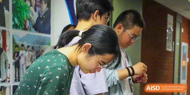 A photo showing a group of students sitting at a desk and studying, at Beijing Foreign Studies University International Curriculum Center.