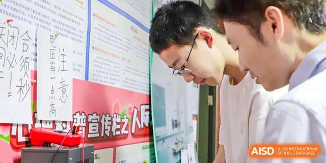 A photo showing a male student standing in front of a poster, at Beijing Foreign Studies University International Curriculum Center.