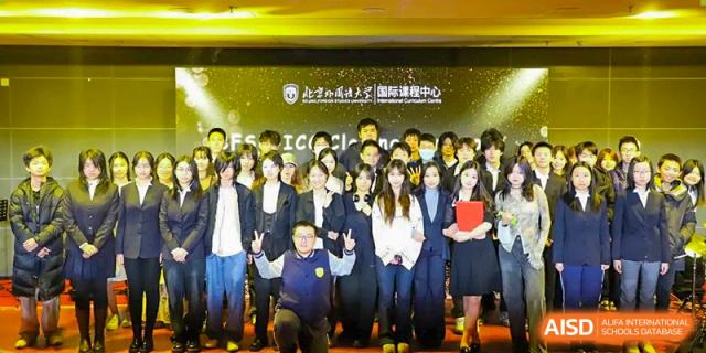 An image showing a large group of people posing for a group photo in front of a stage with a screen, at Beijing Foreign Studies University International Curriculum Center.