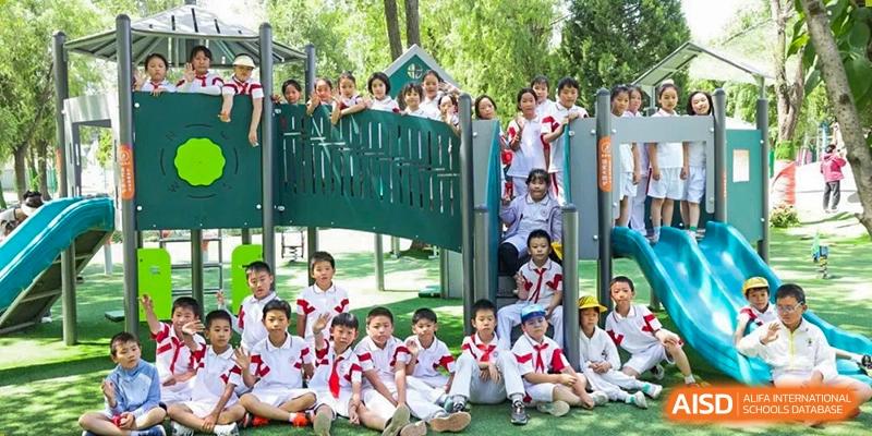 A group of elementary school students from Shijingshan School of The High School Affiliated to Renmin University of China poses for a photo on and around a green playground structure.