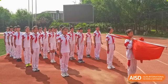 Students from Shijingshan School of The High School Affiliated to Renmin University of China in white tracksuits stand in a line on a track.