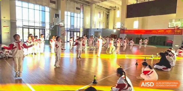 Students from Shijingshan School of The High School Affiliated to Renmin University of China practice martial arts on a polished gym floor.