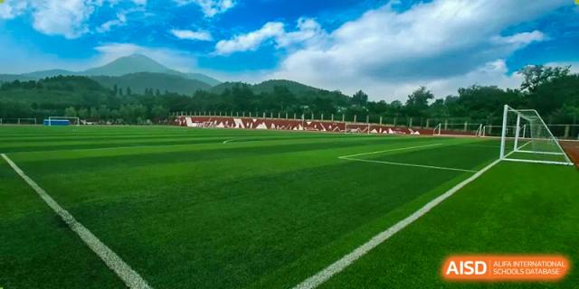 A green sports field at Shijingshan School of The High School Affiliated to Renmin University of China, with students and teachers in the background.