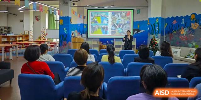 A teacher presenting a colorful slide to an audience of seated parents in a modern school hall. Beanstalk International Bilingual School (BIBS) - Chengdu