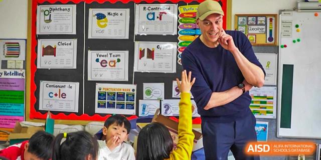 A student raising their hand to answer a question during a lesson with a smiling teacher. Beanstalk International Bilingual School (BIBS) - Chengdu
