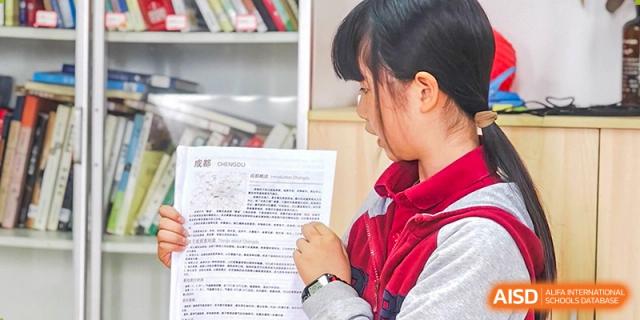 A student carefully reading a printed school document or newsletter in a brightly lit room. Beanstalk International Bilingual School (BIBS) - Chengdu