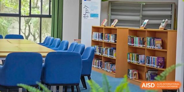 A quiet school library featuring blue chairs and wooden bookshelves filled with various books. Beanstalk International Bilingual School (BIBS) - Chengdu