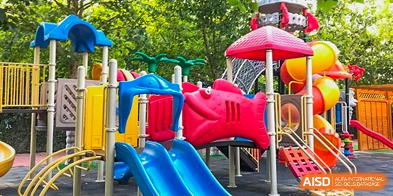 Colorful outdoor playground with blue slides and a red fish-shaped climber under bright sunlight. Beanstalk International Bilingual School (BIBS) - Chengdu