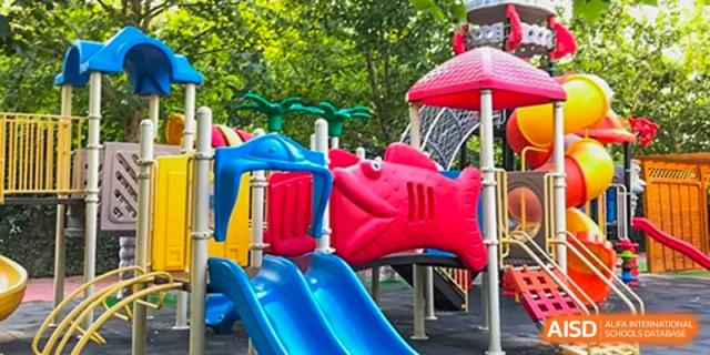 Colorful outdoor playground with blue slides and a red fish-shaped climber under bright sunlight. Beanstalk International Bilingual School (BIBS) - Chengdu