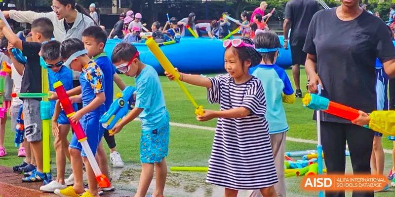 Students laughing and playing with water toys and pool noodles during an outdoor summer water festival. Beanstalk International Bilingual School (BIBS) - Chengdu
