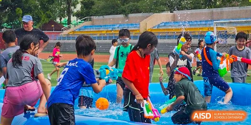 Kids having fun at a splash party, using water guns around a blue inflatable pool on the school field. Beanstalk International Bilingual School (BIBS) - Chengdu