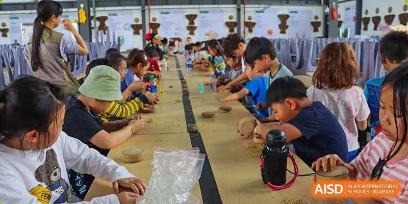 A group of students sitting at a long wooden table, focused on a hands-on craft or science workshop. Beanstalk International Bilingual School (BIBS) - Chengdu