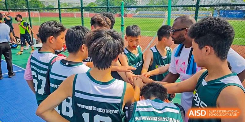 Basketball team in green jerseys huddled together with their coach for a pep talk on the court. Beanstalk International Bilingual School (BIBS) - Chengdu