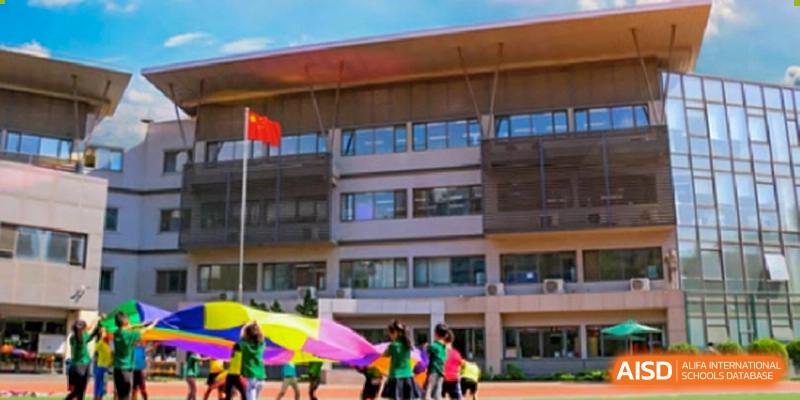 Students playing with a large colorful parachute on the school field in front of the campus building. Beanstalk International Bilingual School (BIBS) - Chengdu