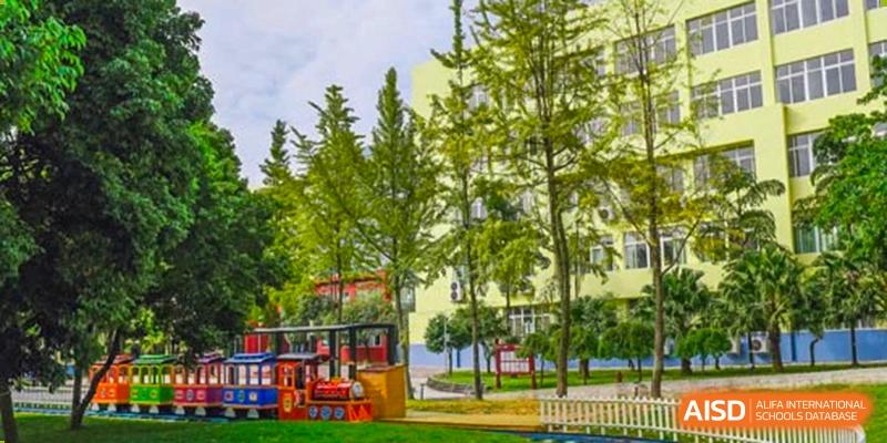 A bright campus view featuring a small red decorative train on a green lawn near leafy trees. Beanstalk International Bilingual School (BIBS) - Chengdu