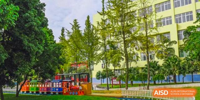 A bright campus view featuring a small red decorative train on a green lawn near leafy trees. Beanstalk International Bilingual School (BIBS) - Chengdu