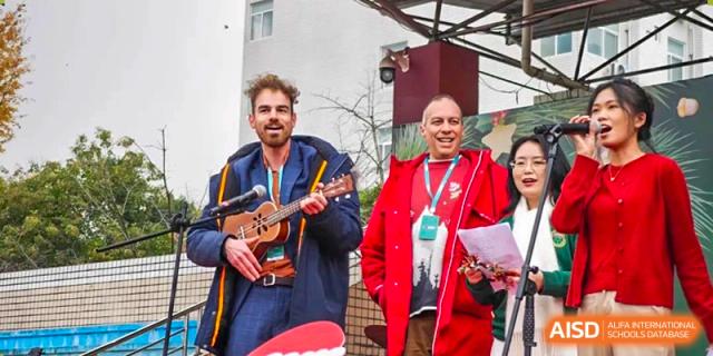 Teachers or staff members smiling and performing with a ukulele during a festive outdoor school event. Beanstalk International Bilingual School (BIBS) - Chengdu