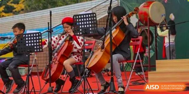 Two students focused on playing cellos during an outdoor musical performance on a red-carpeted stage. Beanstalk International Bilingual School (BIBS) - Chengdu