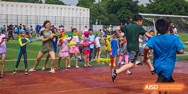 Students running and playing with water blasters during an energetic outdoor splash day on the field. Beanstalk International Bilingual School (BIBS) - Chengdu