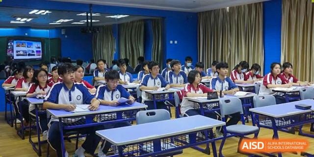 A wide shot of students seated in a classroom with blue walls and a row of empty tables at The Experimental School Affiliated with Zhuhai No.1 High School.