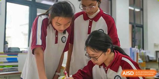 Two female students from The Experimental School Affiliated with Zhuhai No.1 High School in red and white uniforms collaborating on an assignment.