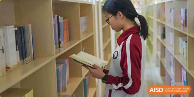A student from The Experimental School Affiliated with Zhuhai No.1 High School standing among bookshelves and reading a book.