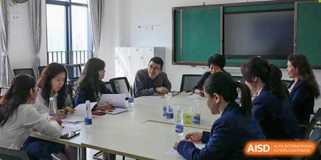 Teachers and students from The Experimental School Affiliated with Zhuhai No.1 High School participating in a small, focused meeting or study group around a table.