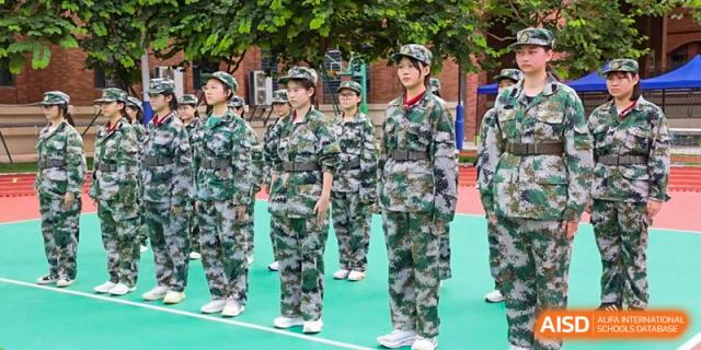 The Experimental School Affiliated with Zhuhai No.1 High School students in camouflage military training uniform standing in formation on a green court.