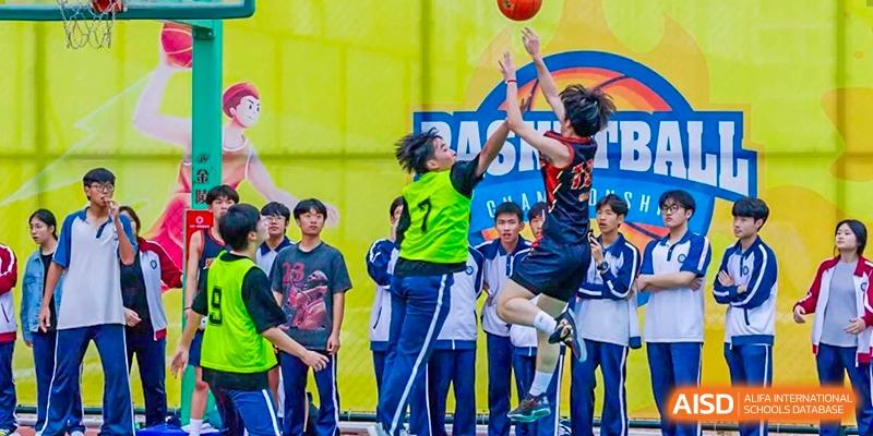 Students from The Experimental School Affiliated with Zhuhai No.1 High School competing in a basketball game, with one player jumping for a shot.