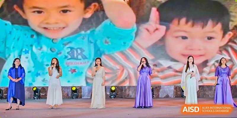 Two singers performing on stage at a ceremony or event for The Experimental School Affiliated with Zhuhai No.1 High School, with one wearing a silver gown and the other a purple gown.
