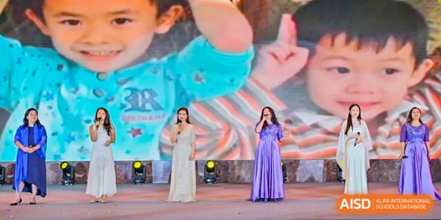 Two singers performing on stage at a ceremony or event for The Experimental School Affiliated with Zhuhai No.1 High School, with one wearing a silver gown and the other a purple gown.